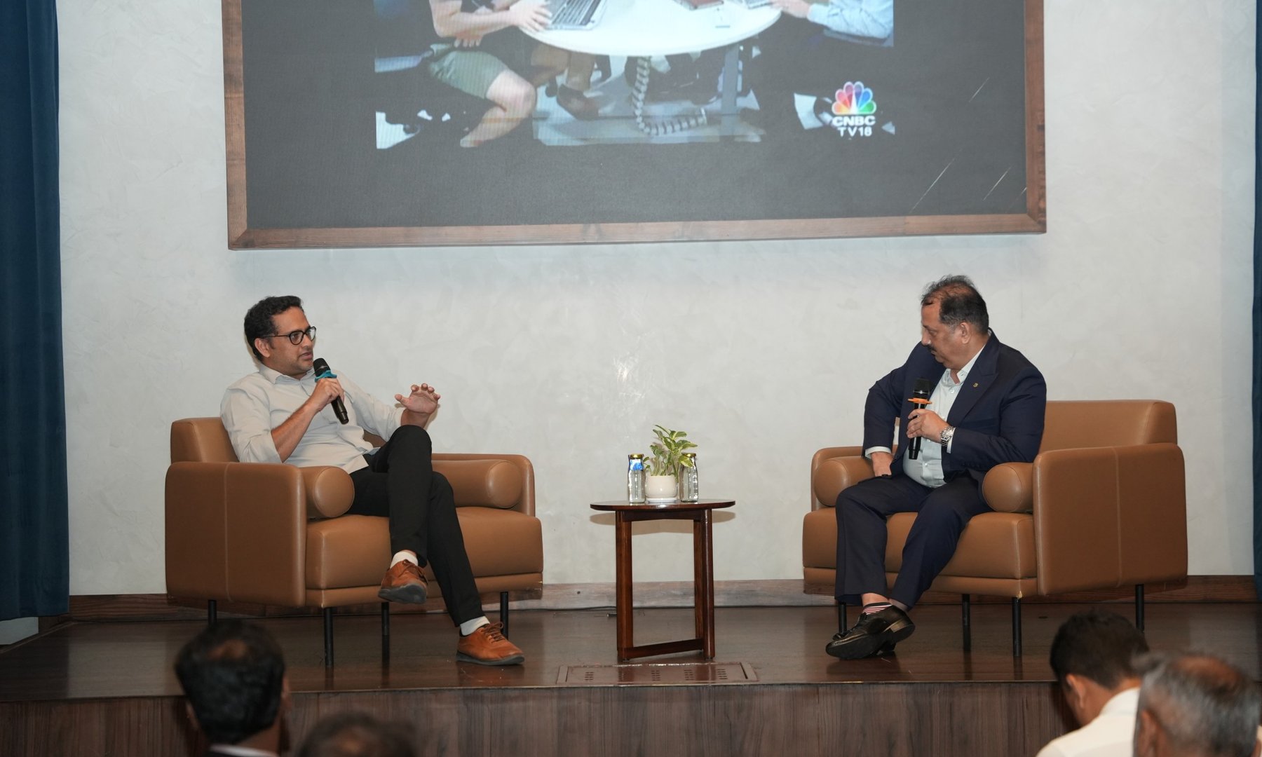 Uday Shetty in a navy suit in a fireside conversation on stage with a guest speaker